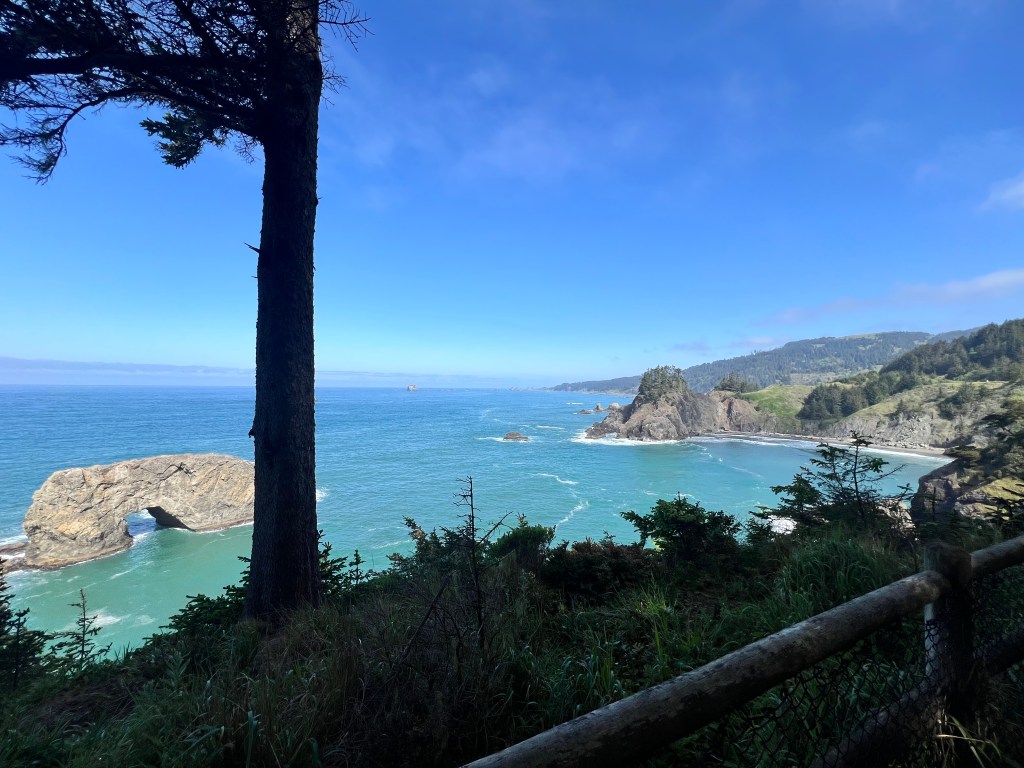 A scenic view of a coastal landscape featuring rocky cliffs, a natural arch in the ocean, and a clear blue sky.